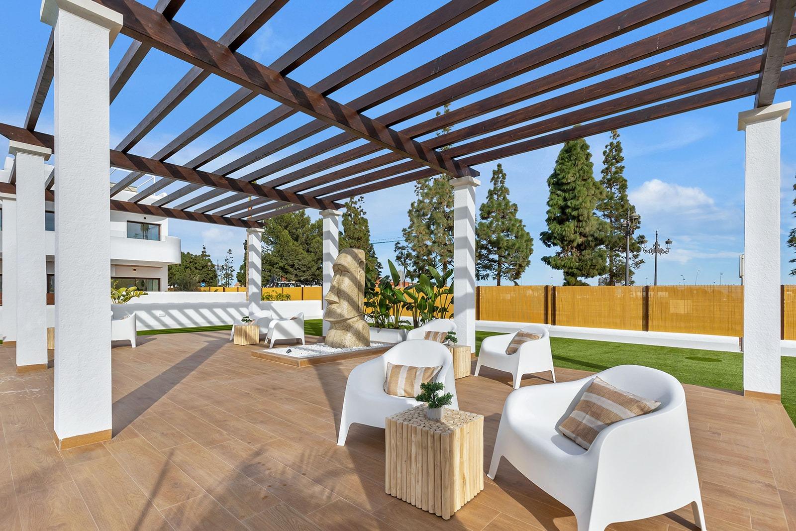 Outdoor lounge area with white curved chairs and beige cushions under a wooden pergola; stone sculpture centerpiece on a tiled patio.