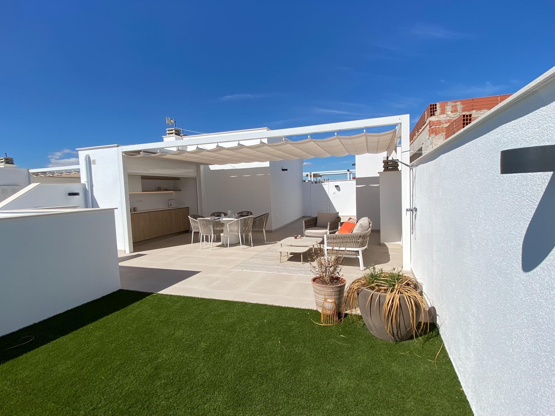Rooftop terrace with white walls, outdoor dining table and sofa set under a beige shade sail, on artificial grass.