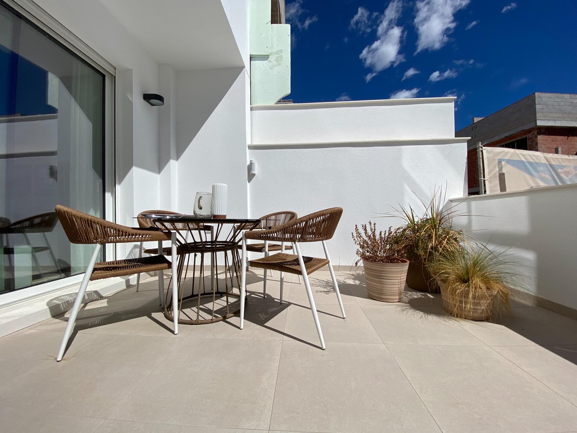 Outdoor terrace with white walls, glass table and brown wicker chairs under a clear blue sky