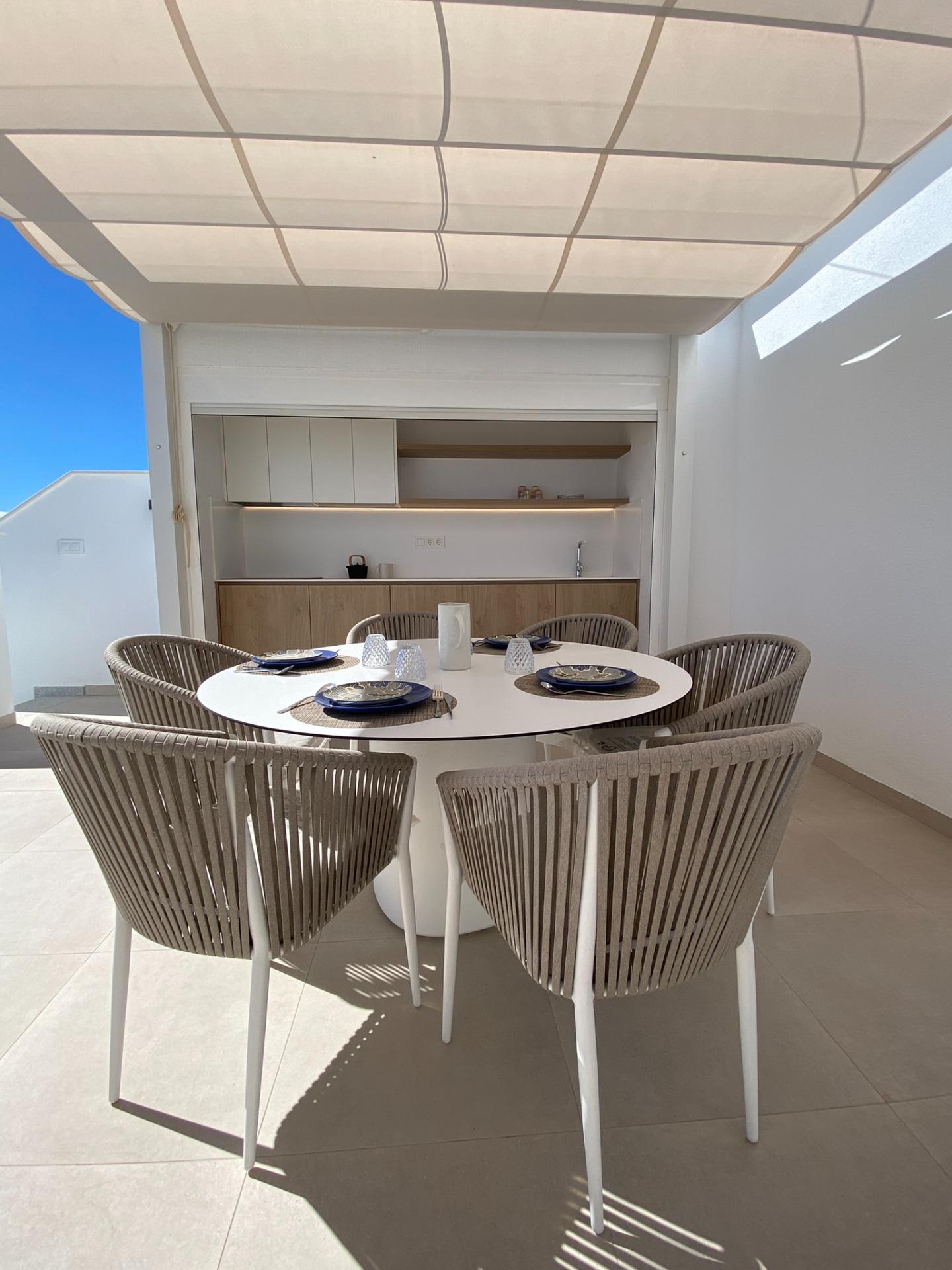 Outdoor dining area with a round white table set with plates and glasses, surrounded by wicker chairs under a fabric canopy.