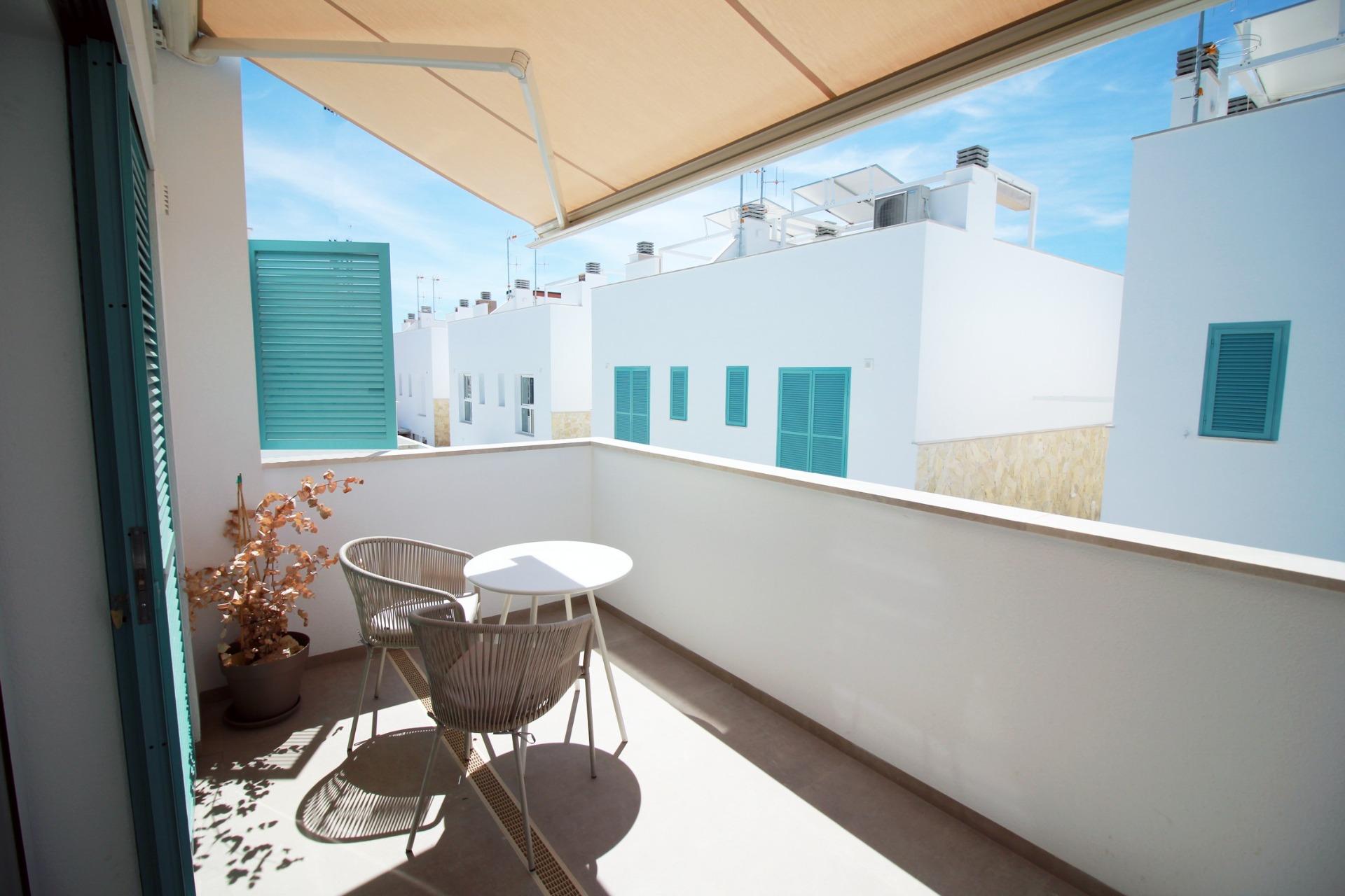 Balcony with a white railing, turquoise window shutters, and a small round table with two chairs under a beige awning.
