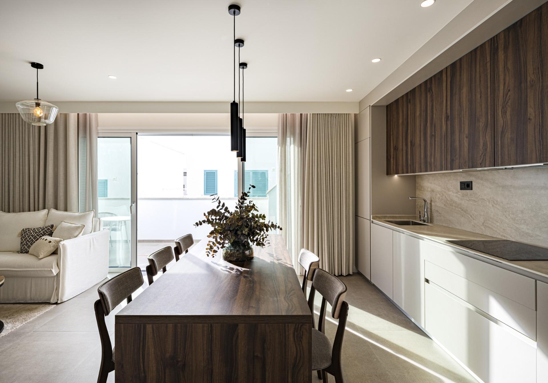 Open-concept dining area with a dark wood table, grey chairs, pendant lights, and a living area with a sofa and curtains nearby.
