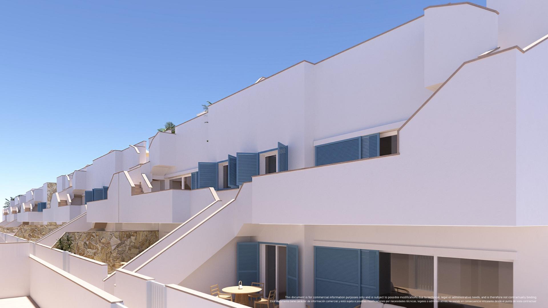 White Mediterranean-style apartment complex with blue shutters and terraced balconies against a clear blue sky.