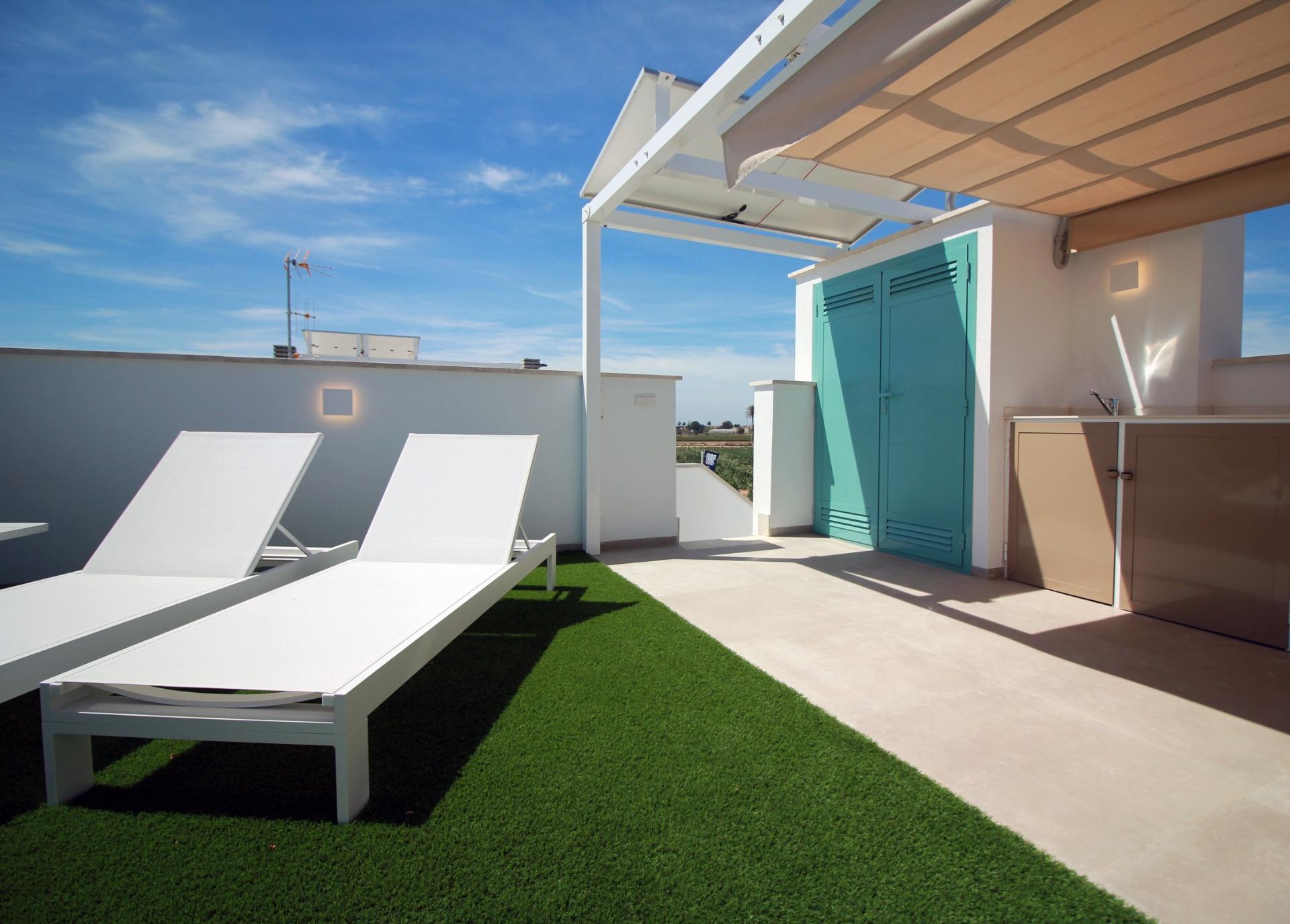 Rooftop terrace with white lounge chairs on green artificial turf and bright turquoise storage doors against a blue sky.