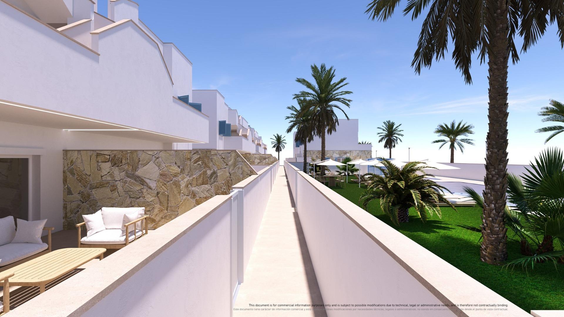 Sunlit resort courtyard with white buildings, a long central walkway, a stone wall on the left, and palm trees with seating areas.