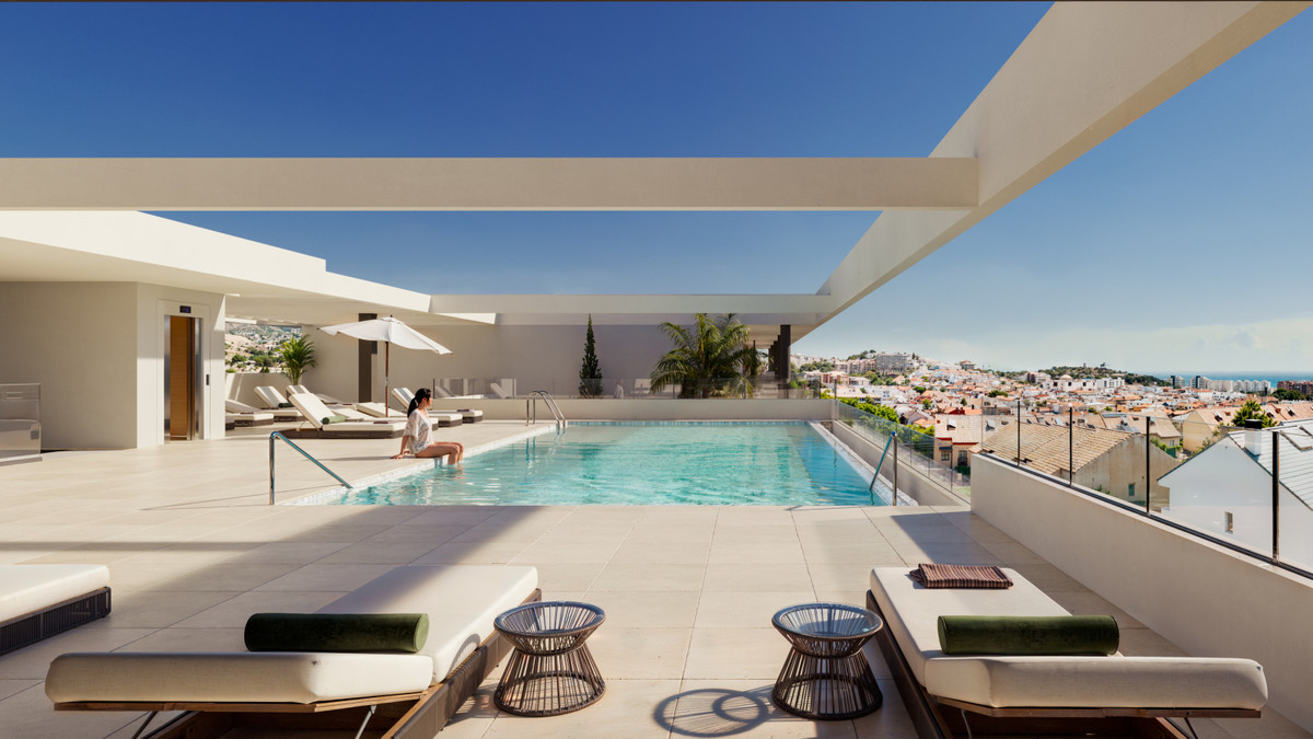 Rooftop pool area with a person sitting at the pool edge, lounge chairs, and a cityscape view under a clear blue sky.
