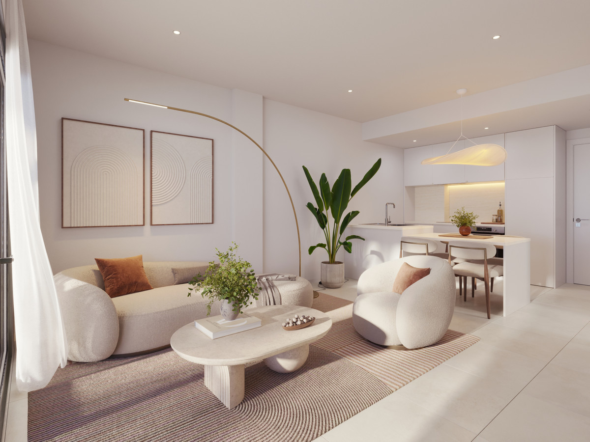Open-plan living area with cream sofas and a round coffee table on a striped rug, a large plant, and a bright kitchen in the background.