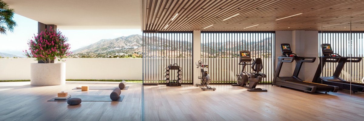 Open-air gym with a wooden ceiling, cardio machines on the right, yoga mats and blocks on the left, and pink flowers in a planter with mountain views beyond.